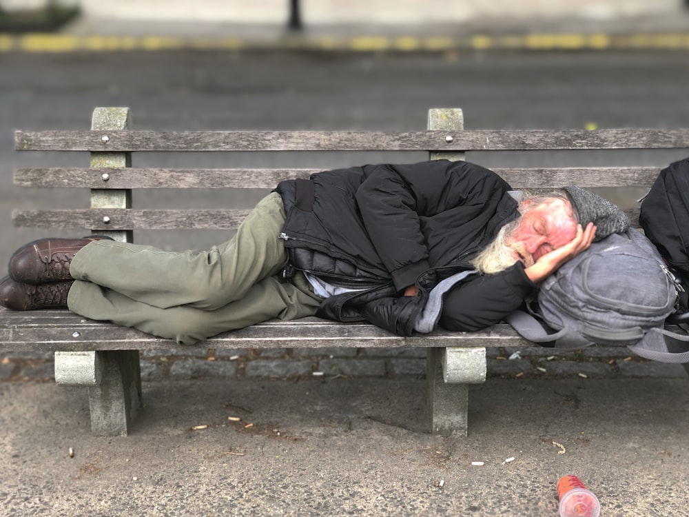 man sleeping on gray wooden bench near outdoor during daytime