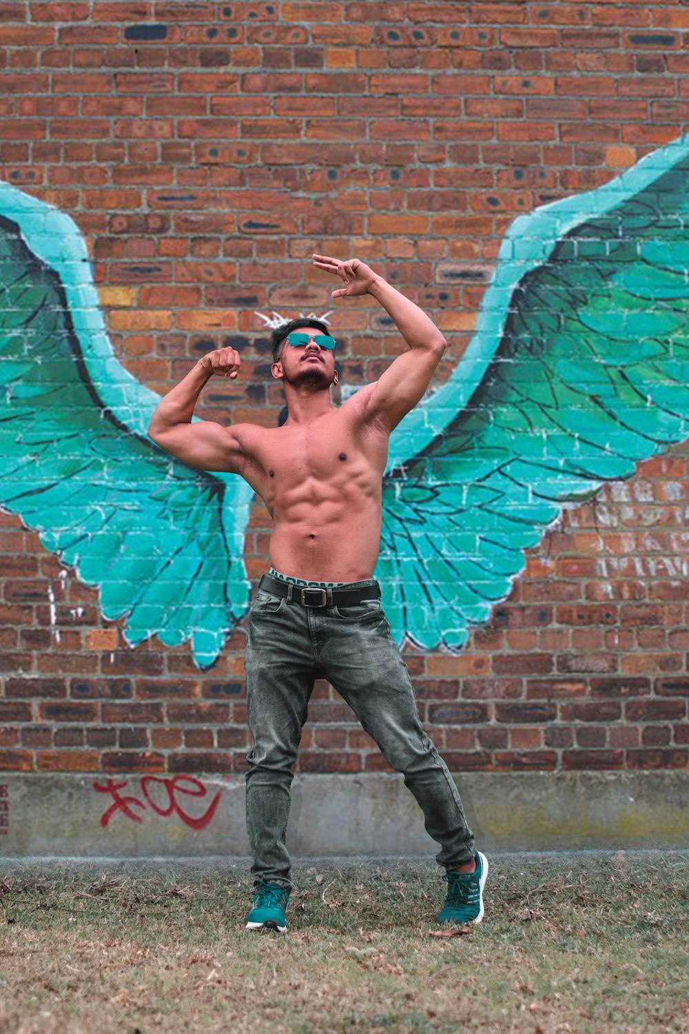 man in front of a painted green wings on brick wall
