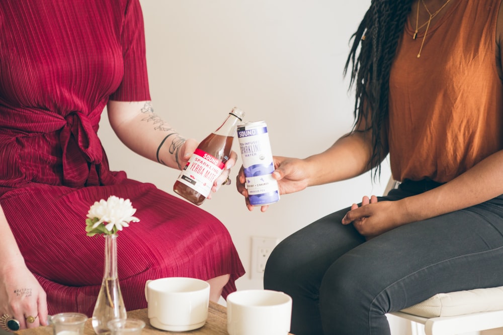 two women holding plastic containers and glass bottles while sitting on chairs