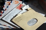 A collection of vintage envelopes is arranged on a flat surface. The top envelope is marked with 'War & Navy Departments V-Mail Service Official Business' and has a torn opening revealing handwritten text inside. Several other envelopes beneath have airmail markings with blue and red stripes, as well as visible handwritten addresses.