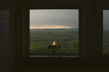 Softly lit candle flickering beside a window overlooking Corsican landscape.