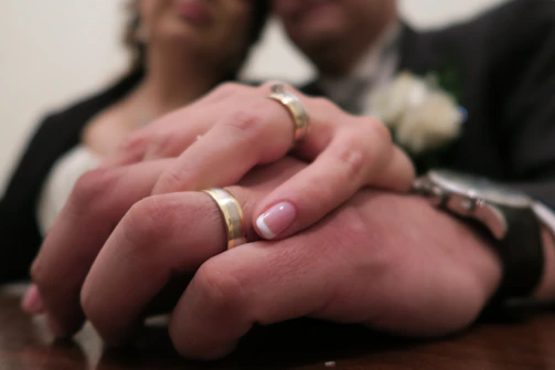 A close-up of intertwined hands, wedding rings gleaming, with camels in the background.
