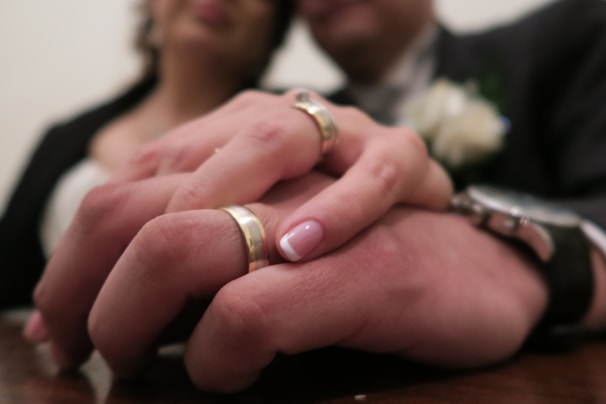 A close-up of intertwined hands adorned with traditional wedding rings.