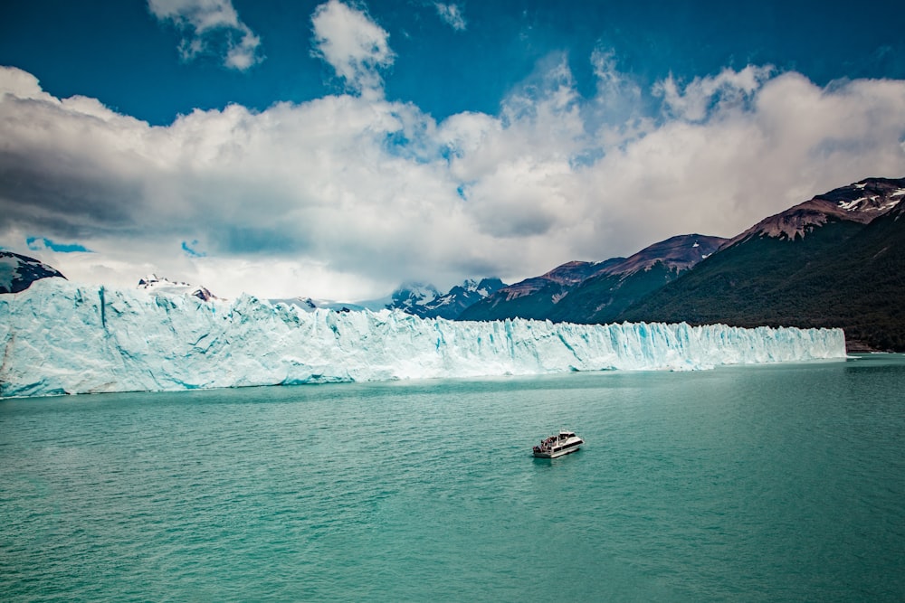 Photographie aérienne d’un bateau blanc sur un plan d’eau à côté d’une falaise de blocs de glace pendant la journée