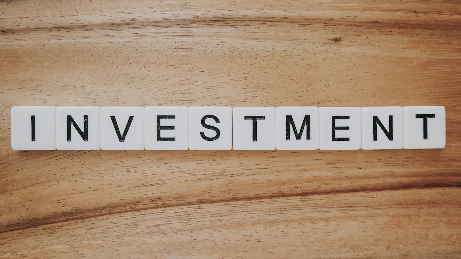 Buchstabensteine formen das Wort Investment auf einer Holzoberfläche