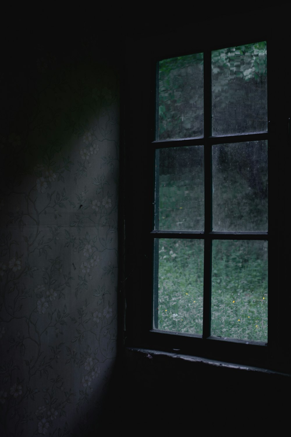 a window in a dark room with a wallpapered wall