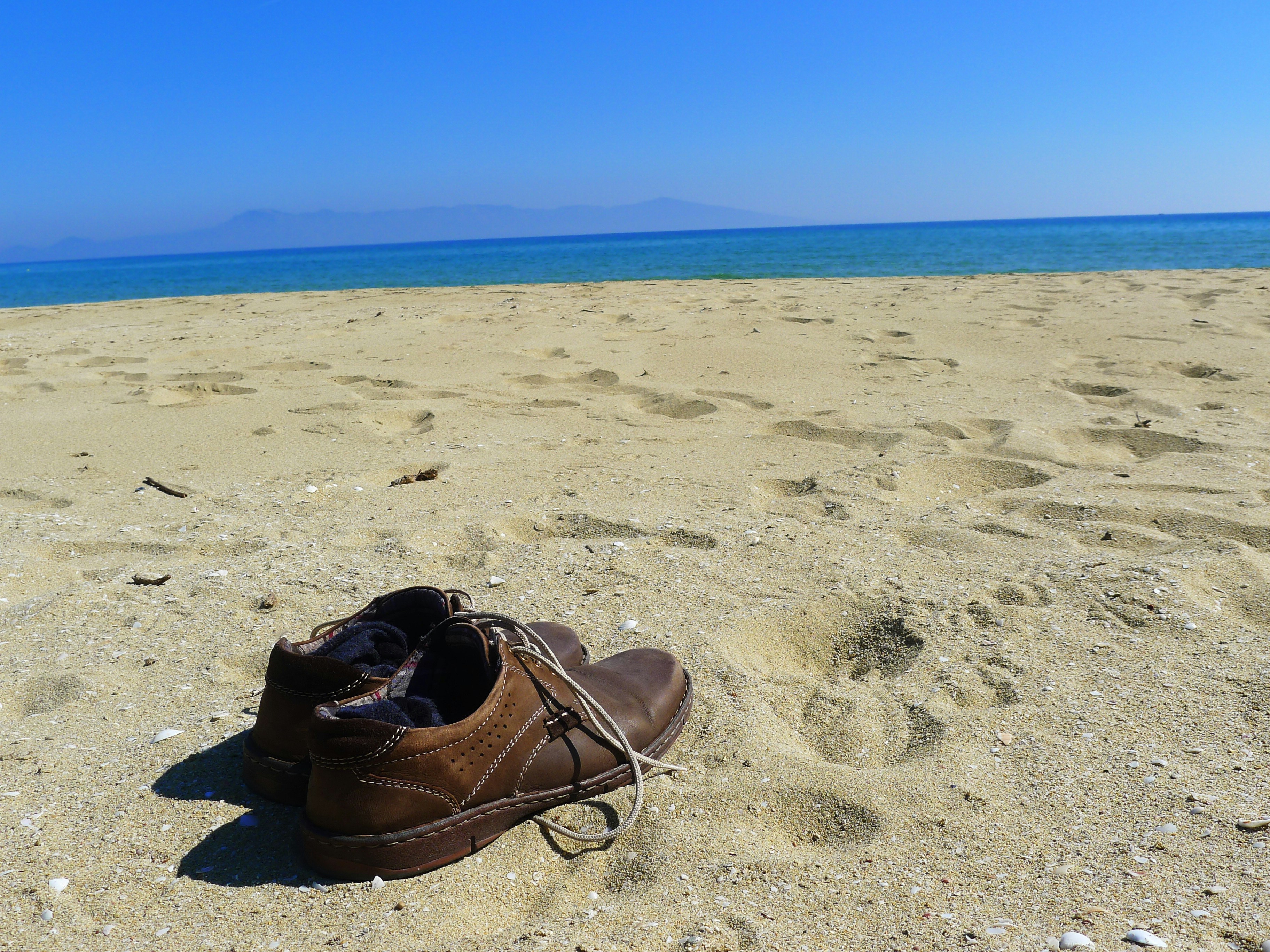 pair of brown leather shoes on white sand