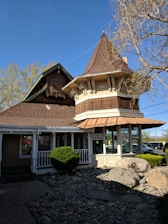 A quaint building with a unique architectural design featuring a turret and wooden elements, surrounded by a small landscaped area with rocks and bushes. There are signs in the windows indicating a car wash service.