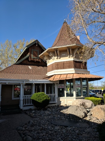 A quaint building with a unique architectural design featuring a turret and wooden elements, surrounded by a small landscaped area with rocks and bushes. There are signs in the windows indicating a car wash service.