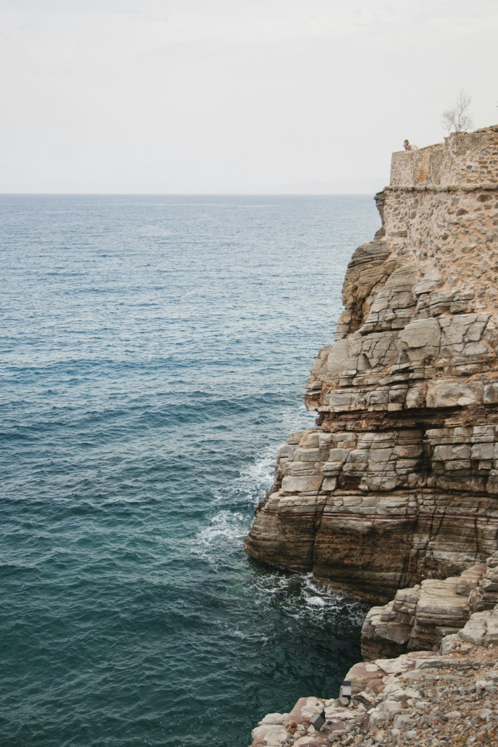 person sitting on cliff while watching sea