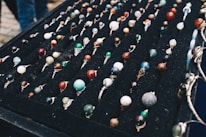 A display of numerous handcrafted rings, each featuring a unique, colorful gemstone set in silver wire wrapping, arranged neatly on a black velvet board. The stones vary in color and pattern, creating an artistic and vibrant presentation.
