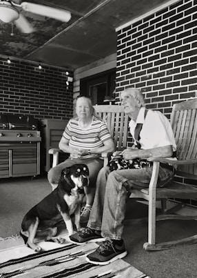 grayscale of man and woman sitting on wooden rocking chairs