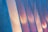 Vertical panels with a textured surface are illuminated by soft, warm light creating a gradient of colors including blue, pink, and orange. The surface texture resembles rough concrete, giving a modern architectural feel.