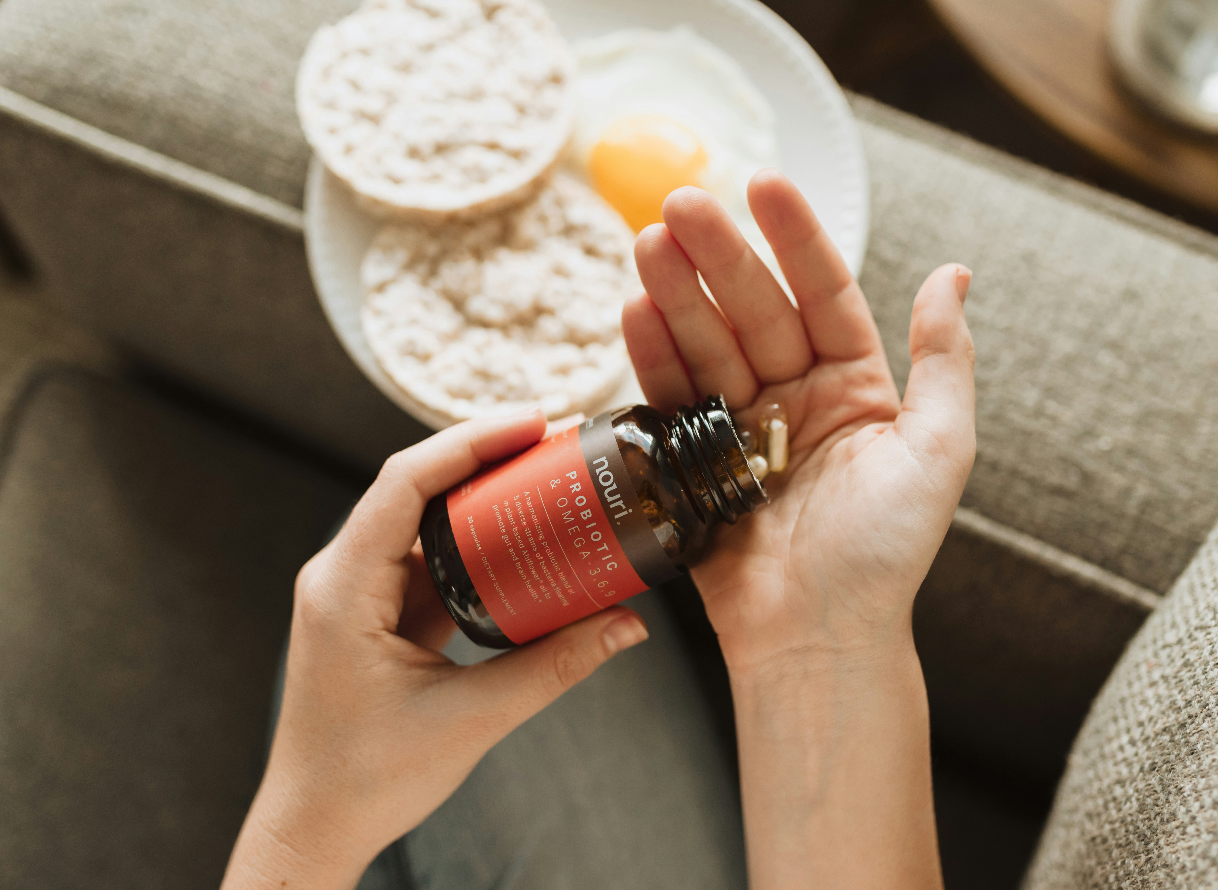 Woman taking supplements in the morning. A plate of breakfast remains in the background. Woman puts probiotic capsule pills into her hand for her morning health care routine.