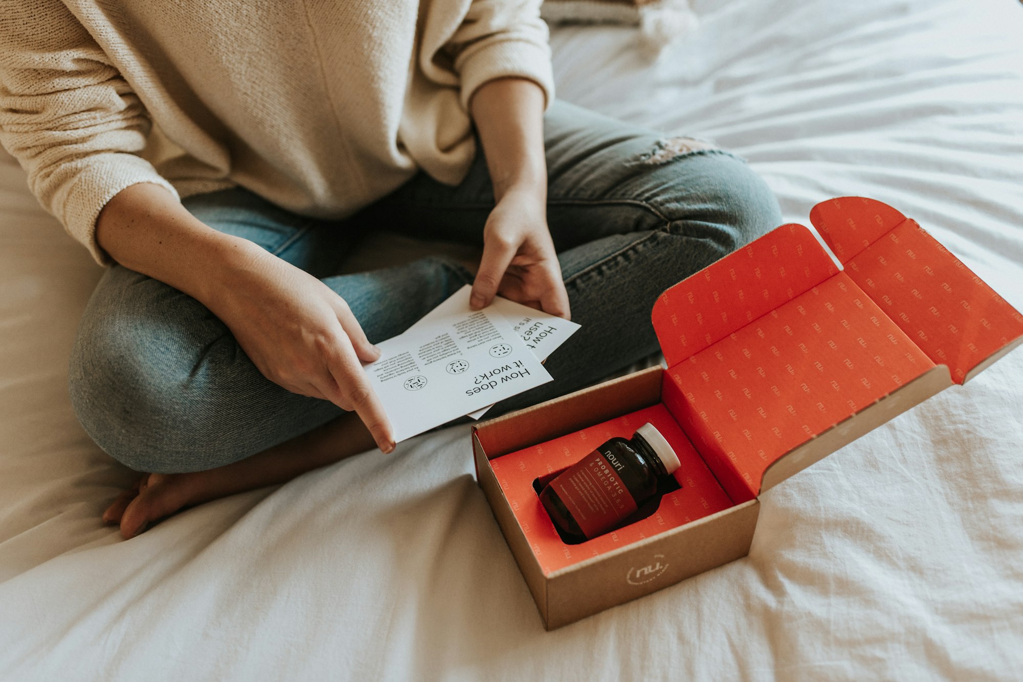 Woman sitting on bed while reading package materials included within the Nouri subscription box. 