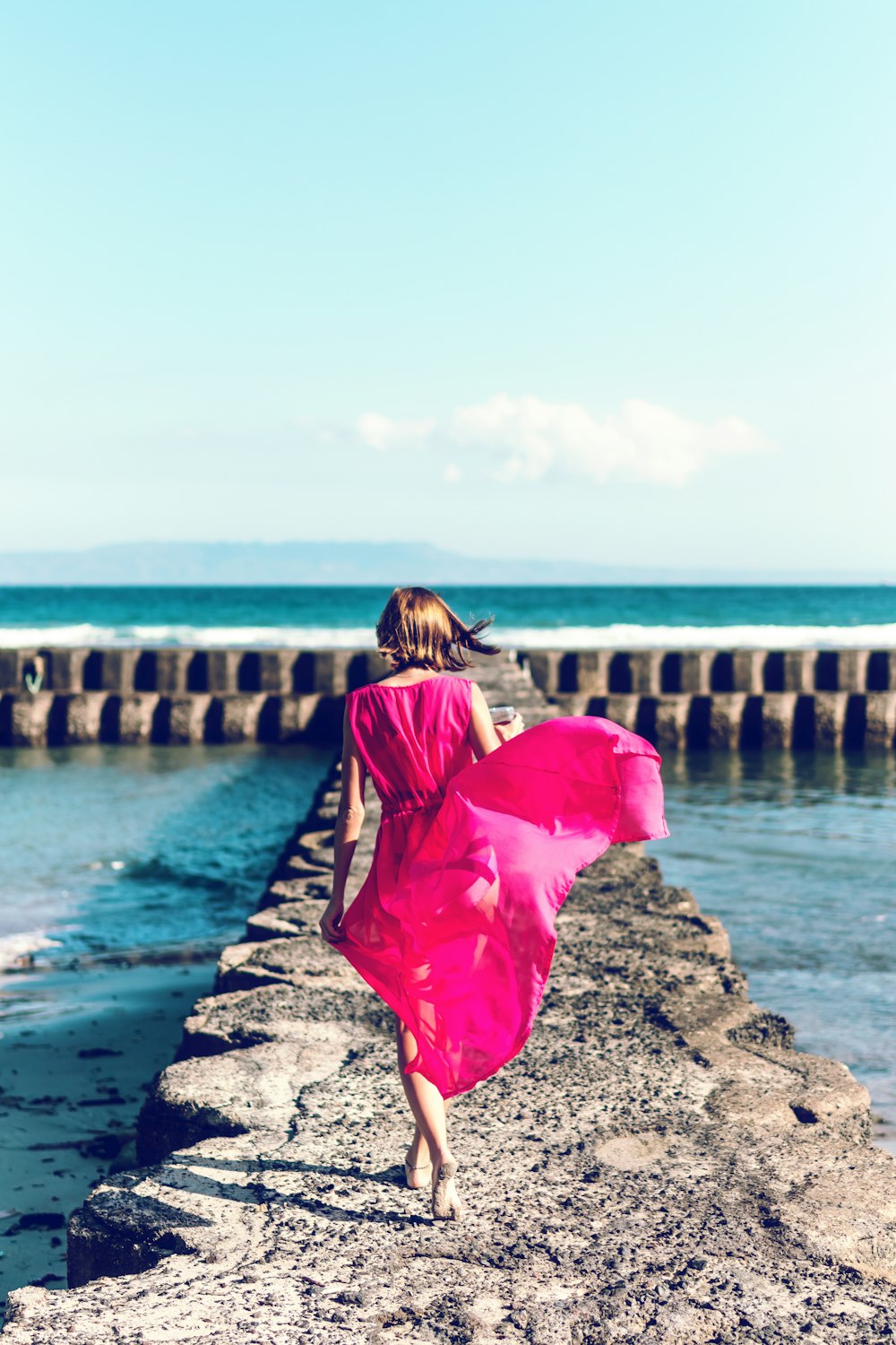 Frau im rosafarbenen ärmellosen Kleid am Ufer spazieren