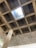 A concrete ceiling features a grid layout with a central square opening allowing light to enter. The structure reveals visible formwork patterns, creating a textured appearance. A vertical concrete column supports the ceiling.