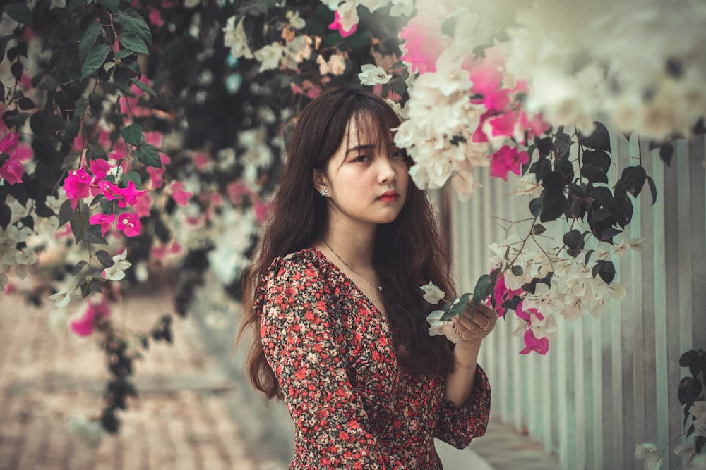 woman wearing red and gray floral dress surrounded by flowers