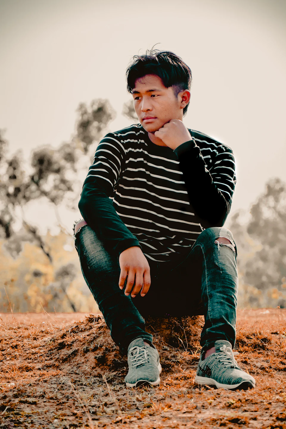 Young man sits on a rock with his legs crossed and hands on knees
