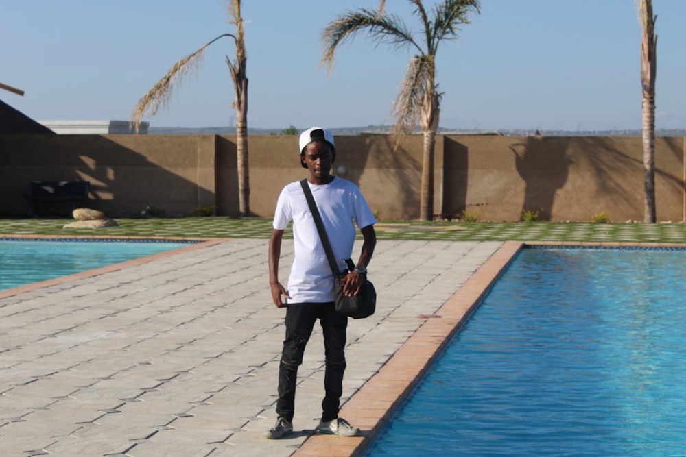 man in white t-shirt and black pants standing beside swimming pool