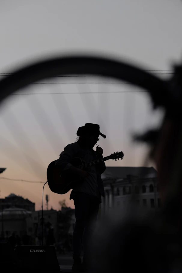 silhouette of man wearing cowboy hat while holding guitar