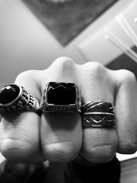 A close-up of a hand adorned with gold rings against a dark textured background.