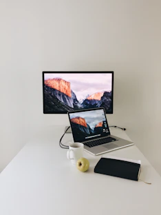 A minimalist workspace with a sleek laptop, a navy-blue notebook, and a cup of coffee beside a window overlooking Dhaka's skyline.