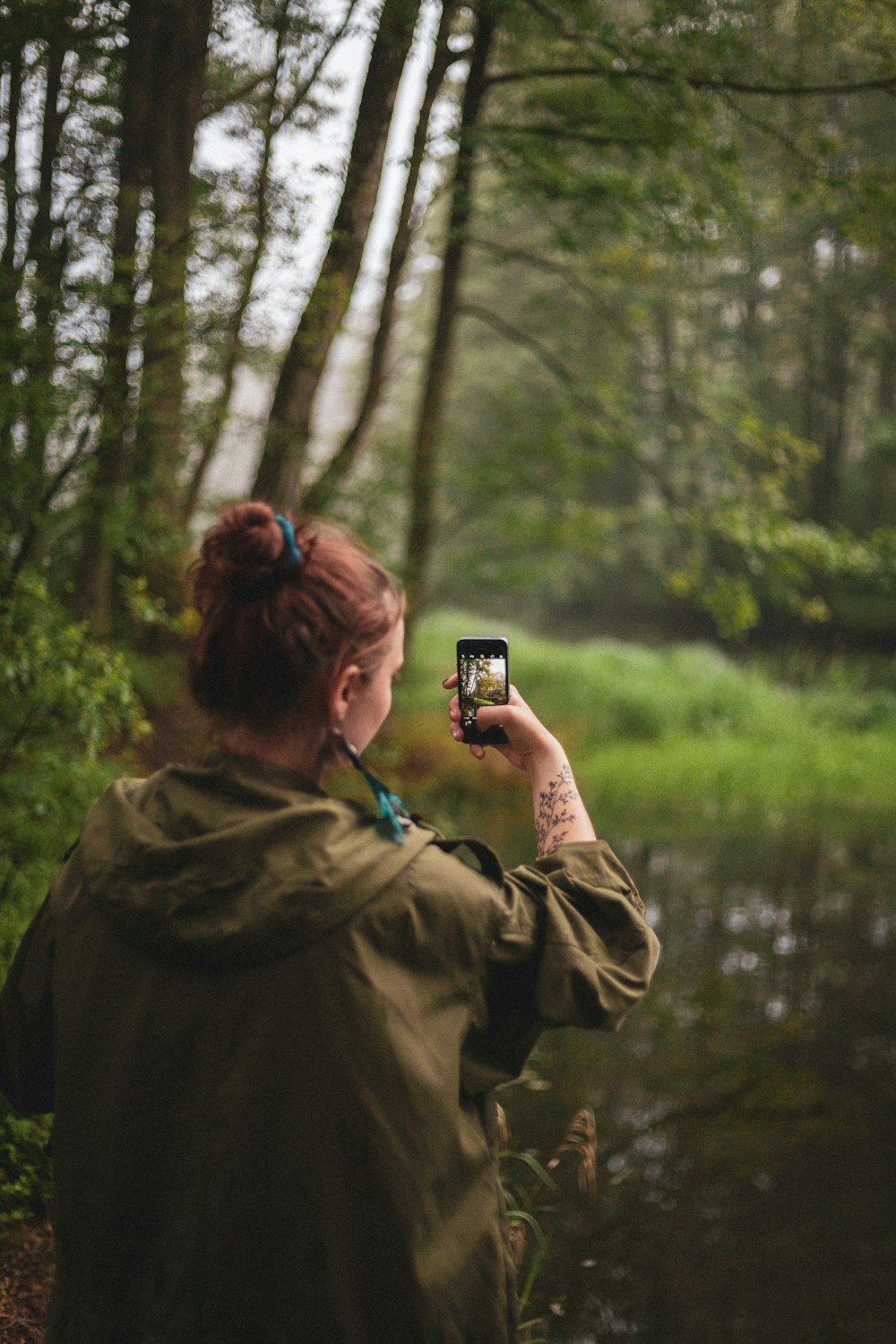 woman wearing jacket taking photo of trees