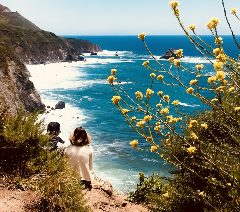 couple sitting on hill in front of body of water