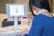 A woman interacts with a digital check-in kiosk that features a tablet screen displaying a user's profile image and a 'Confirm' button. She seems to be verifying her identity or checking in for an event or appointment. The setting suggests a modern office or reception area.