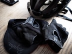 A cycling helmet and gloves are placed on a wooden surface, along with a cap featuring a visible logo. The items appear neatly arranged, suggesting preparedness for a cycling activity.