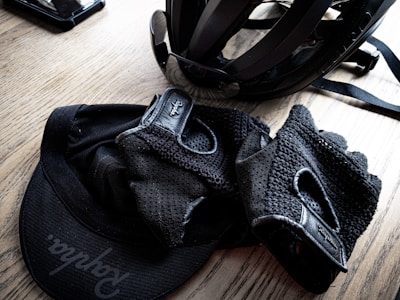 A cycling helmet and gloves are placed on a wooden surface, along with a cap featuring a visible logo. The items appear neatly arranged, suggesting preparedness for a cycling activity.