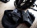 A cycling helmet and gloves are placed on a wooden surface, along with a cap featuring a visible logo. The items appear neatly arranged, suggesting preparedness for a cycling activity.
