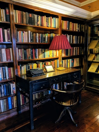 A cozy writing desk with an open notebook, a vintage pen, and soft natural light highlighting a stack of classic literature books.