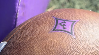 A close-up of a football with a blurred stadium background.