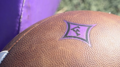 A close-up of a football with a blurred stadium background.
