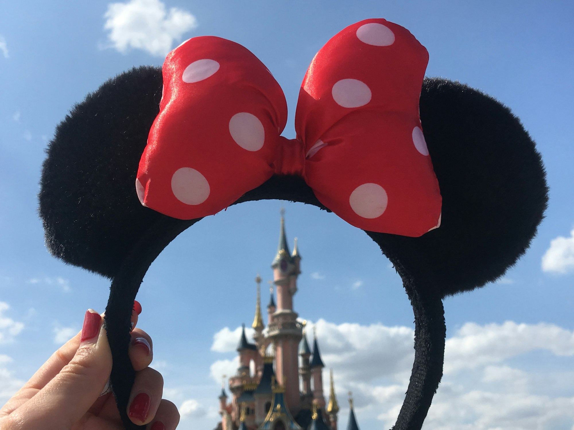 A woman holds a pair of Minnie Mouse ears in front of the Disney castle