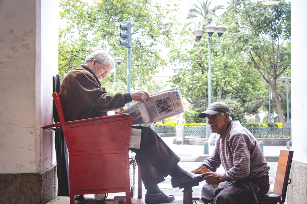 man doing shoe shine of man in brown jacket sitting on red chair