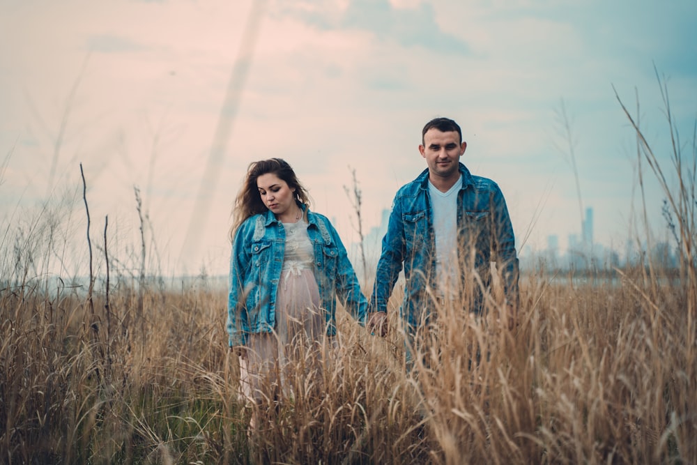 man and woman in blue denim jackets walking in brown grass field hand in hand