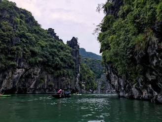 A colorful boat glides past towering limestone cliffs covered in vibrant greenery.