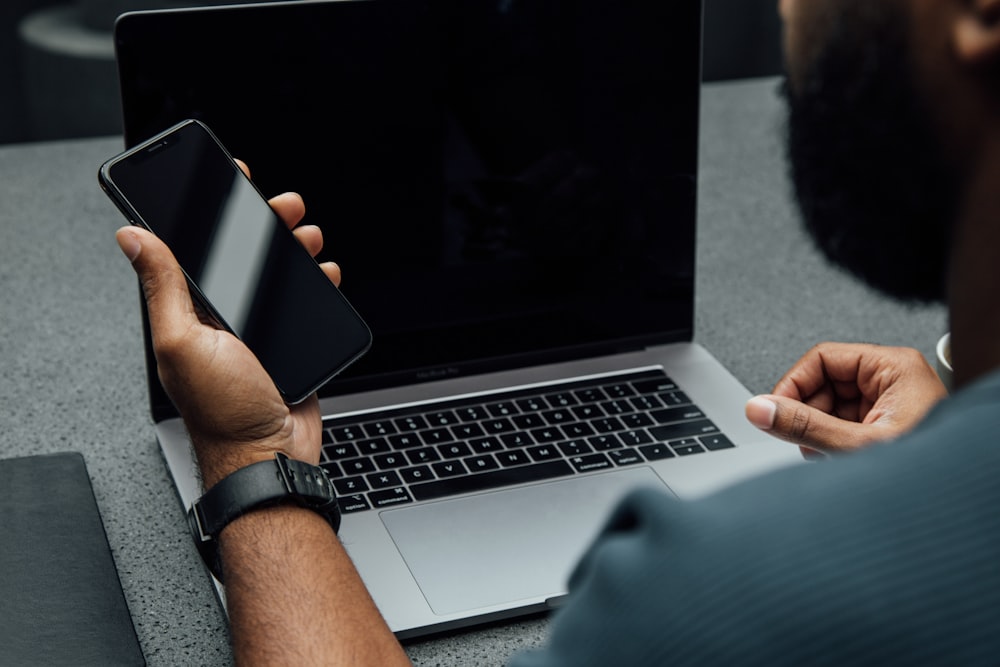 person holding iPhone using left hand near MacBook Pro