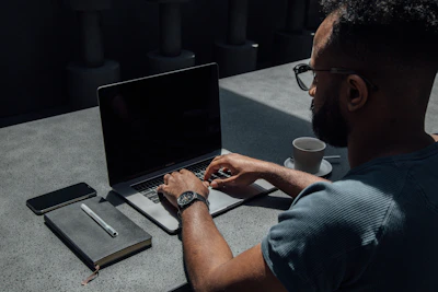 Social media manager working intently on a laptop with notes and coffee nearby, framed by soft natural light.
