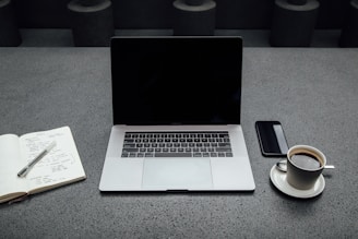 turned-off MacBook Pro between cup of coffee, iPhone, notebook, and pen
