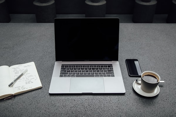 A neat workspace with a laptop displaying a clear financial dashboard, surrounded by a notebook and a cup of coffee.