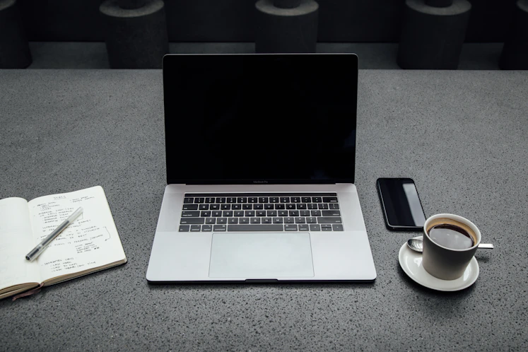A sleek, modern workspace with a laptop, coffee cup, and a notepad ready for notes.