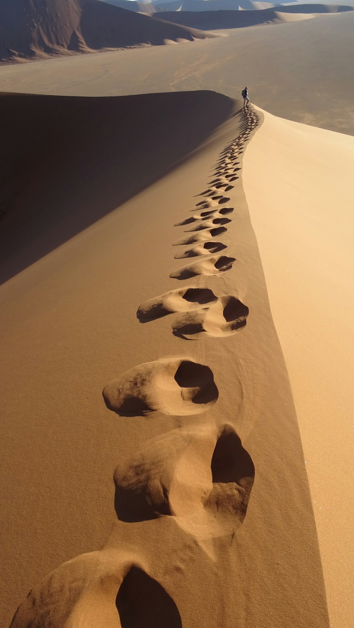 Pegadas na areia do deserto — uma trilha solitária que atravessa as dunas, marcando o caminho percorrido