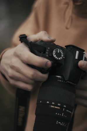 Hands adjusting the focus ring on a black camera with gold accents.
