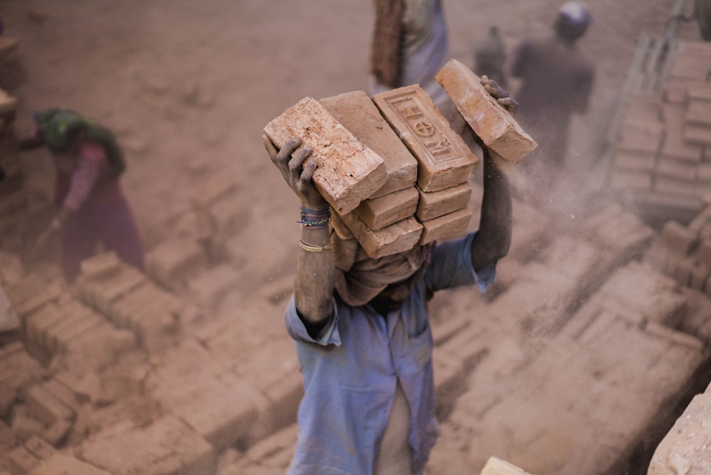 man in blue shirt carrying blocks on head