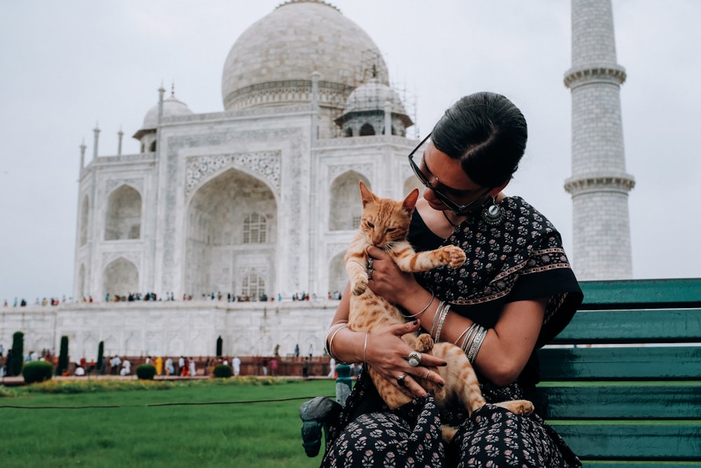 woman carrying orange tabby cat across white mosque