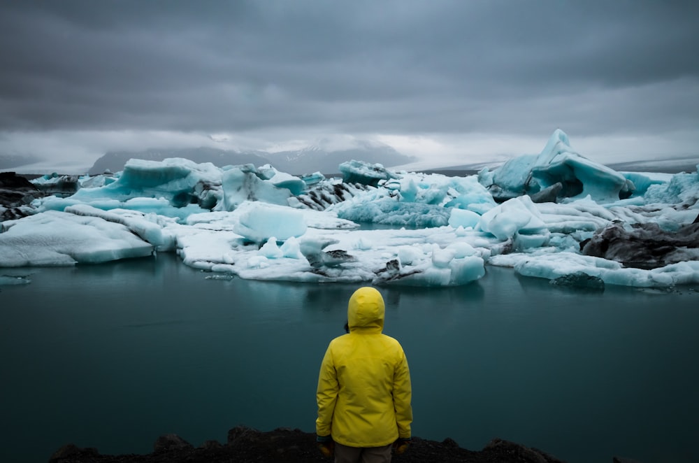 person standing facing sea covered with snow under gray skies